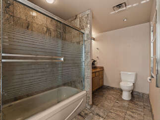 This bathroom features a luxurious bathtub with a frosted glass enclosure, complemented by elegant granite tilework on the walls and floors.