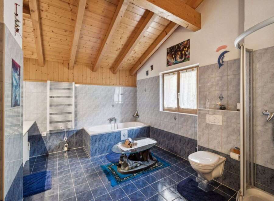 This charming bathroom features a vaulted wooden ceiling and elegant blue and grey tiled walls.