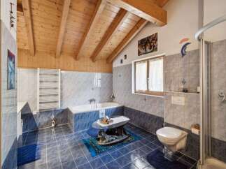 This charming bathroom features a vaulted wooden ceiling and elegant blue and grey tiled walls.