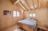 Experience cozy living in this charming wooden cabin bedroom, featuring a comfortable bed with striped bedding and natural light streaming through two windows.