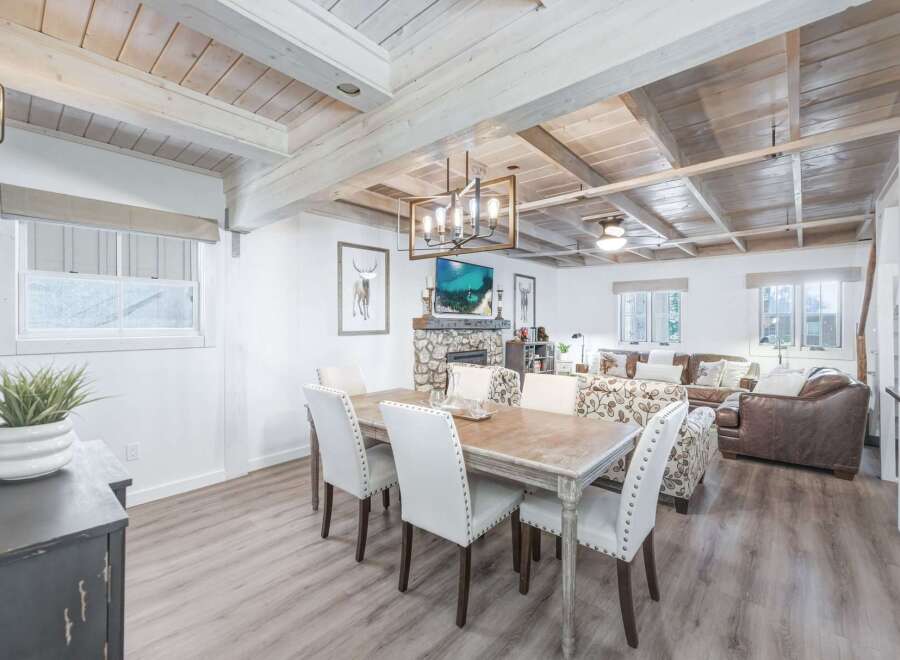 Experience rustic charm in this open-concept living space, featuring a cozy stone fireplace and a stylish dining area with upholstered chairs.