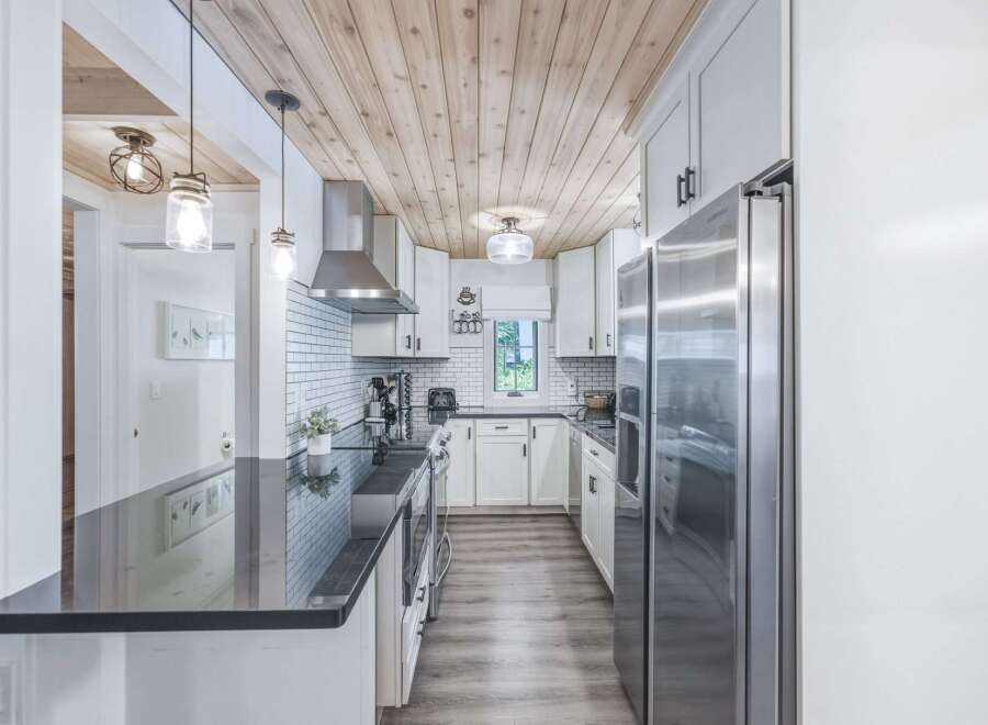 This modern kitchen boasts a stunning wood-planked ceiling, complemented by sleek white cabinetry and a durable granite countertop.