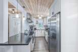This modern kitchen boasts a stunning wood-planked ceiling, complemented by sleek white cabinetry and a durable granite countertop.