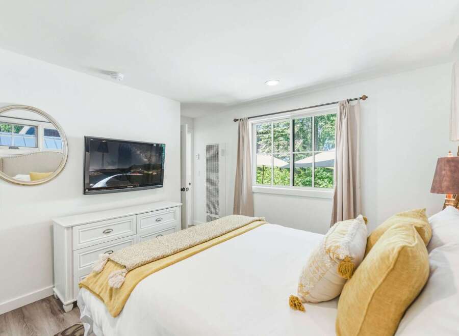 Experience comfort and style in this beautifully appointed bedroom, featuring a wall-mounted TV above a classic white dresser.