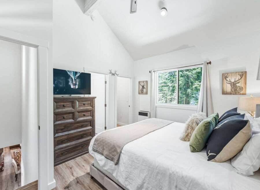 Experience rustic charm in this inviting bedroom, featuring a vaulted ceiling and a large window with serene forest views.