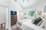 Experience rustic charm in this inviting bedroom, featuring a vaulted ceiling and a large window with serene forest views.