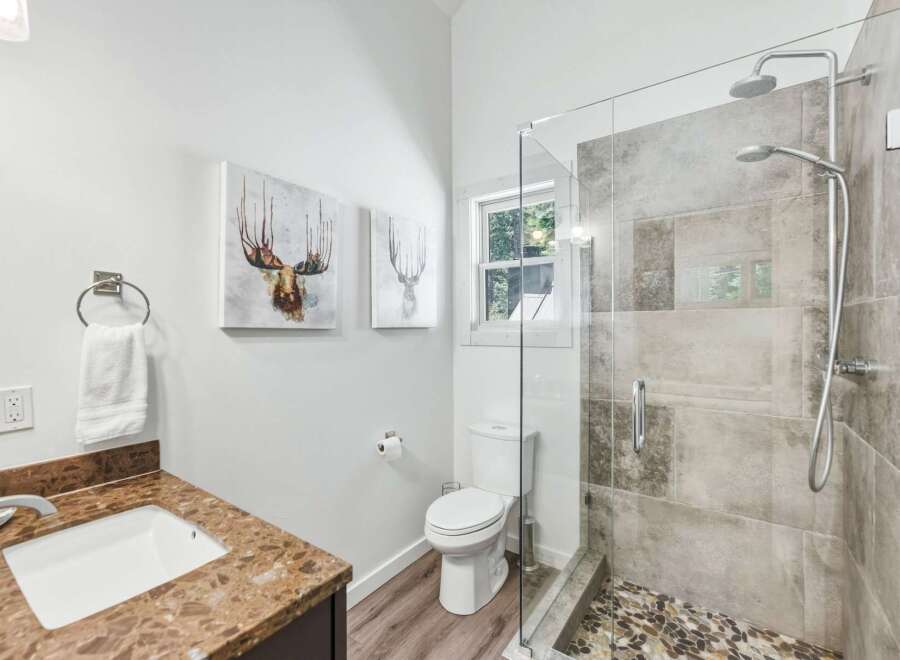 This modern bathroom features a sleek glass-enclosed shower with a dual showerhead and pebble tile flooring.