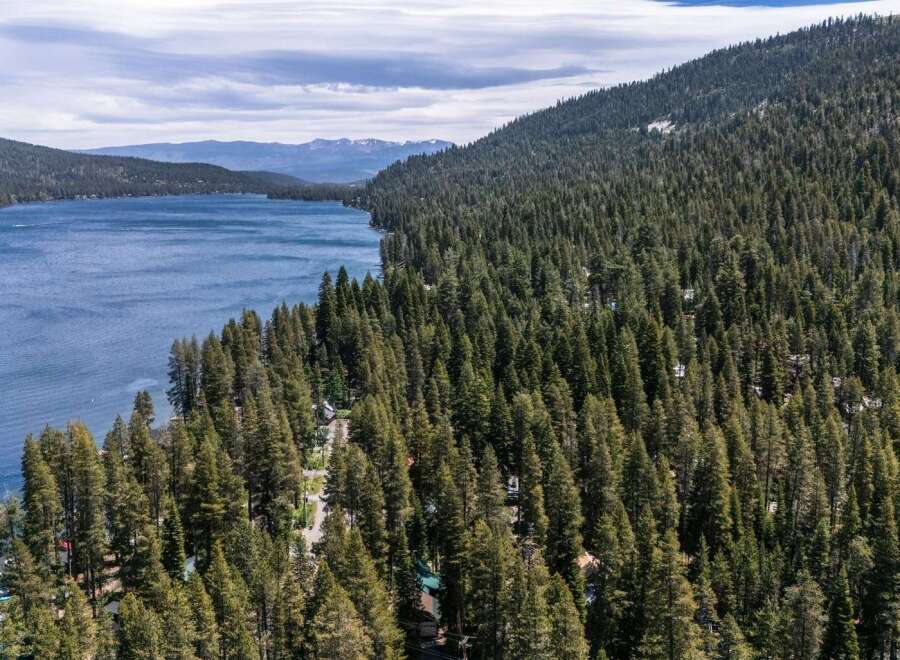 Experience the ultimate lakeside living with this stunning aerial view of a property nestled amidst a dense pine forest, offering breathtaking views of a serene blue lake.