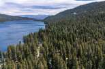 Experience the ultimate lakeside living with this stunning aerial view of a property nestled amidst a dense pine forest, offering breathtaking views of a serene blue lake.