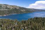 Experience the ultimate lakeside living with this stunning aerial view of homes nestled among pine trees, offering breathtaking vistas of a vast, blue lake.