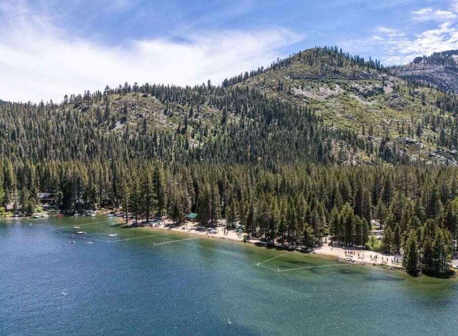 Experience lakeside living with this stunning aerial view of a serene lake surrounded by a dense forest and majestic mountains.