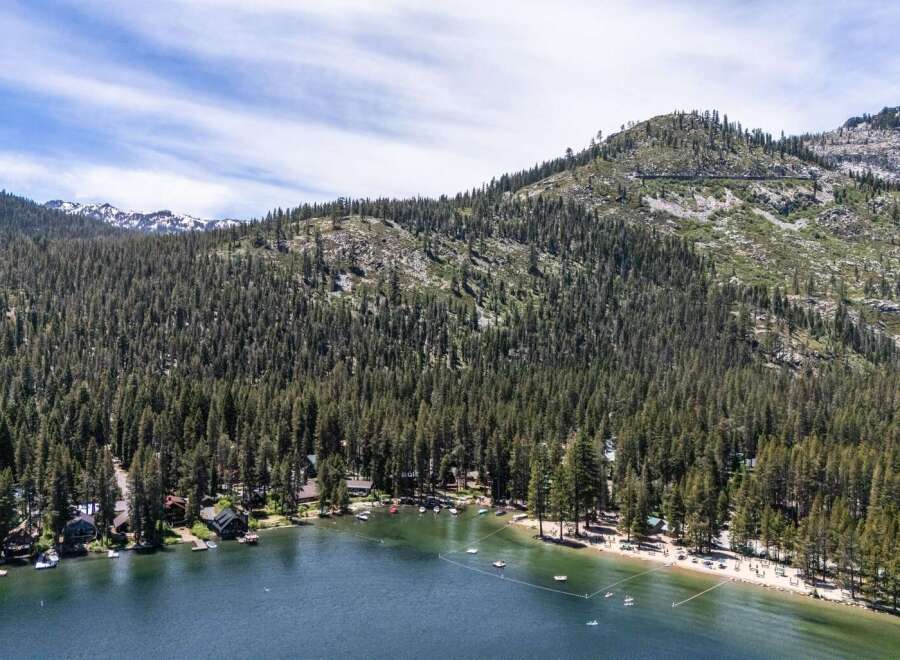 Experience the ultimate lakeside living with this stunning aerial view of homes nestled along a pristine lake, surrounded by a dense forest and majestic mountains.