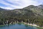 Experience the ultimate lakeside living with this stunning aerial view of homes nestled along a pristine lake, surrounded by a dense forest and majestic mountains.