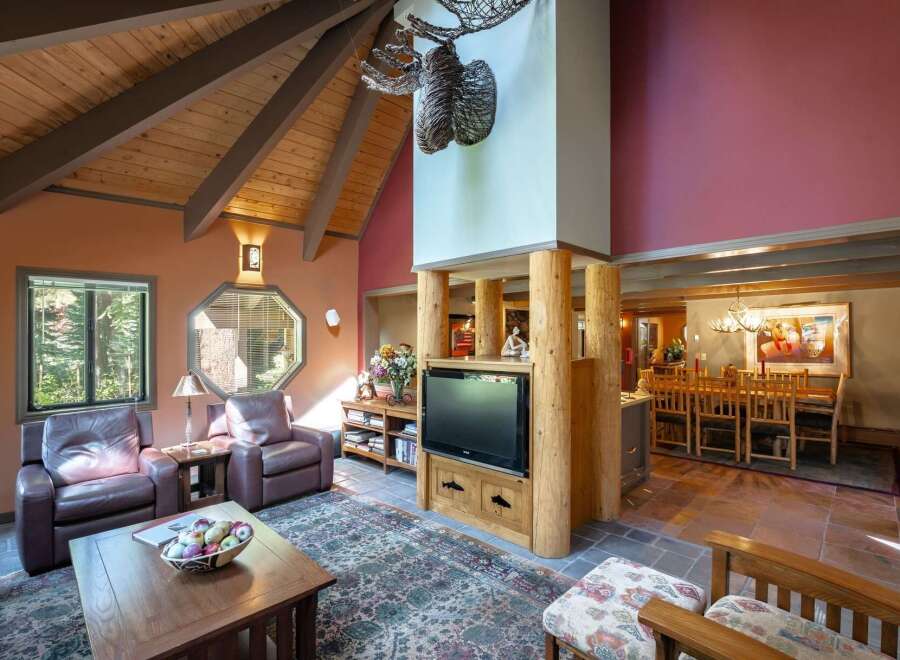Experience rustic charm in this spacious living area featuring a vaulted wood-beamed ceiling and a striking moose antler chandelier.