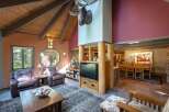 Experience rustic charm in this spacious living area featuring a vaulted wood-beamed ceiling and a striking moose antler chandelier.