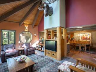 Experience rustic charm in this spacious living area featuring a vaulted wood-beamed ceiling and a striking moose antler chandelier.