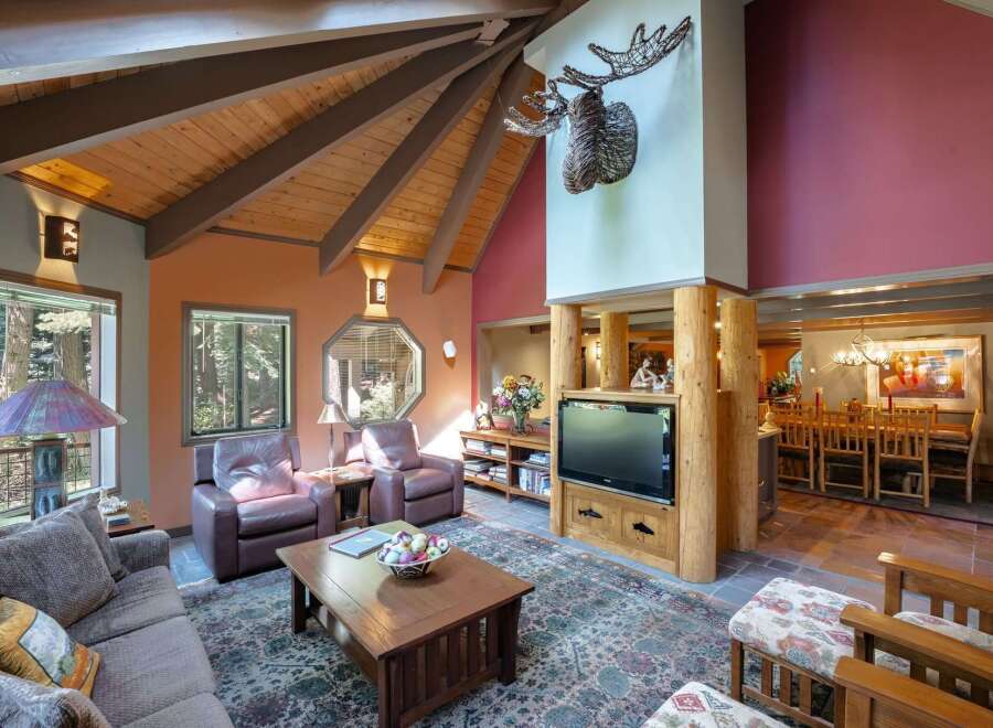 Experience rustic charm in this spacious living area, featuring a vaulted wood-beamed ceiling and a striking mounted antler decor.