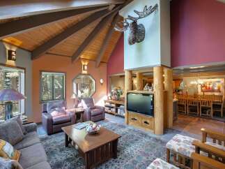 Experience rustic charm in this spacious living area, featuring a vaulted wood-beamed ceiling and a striking mounted antler decor.