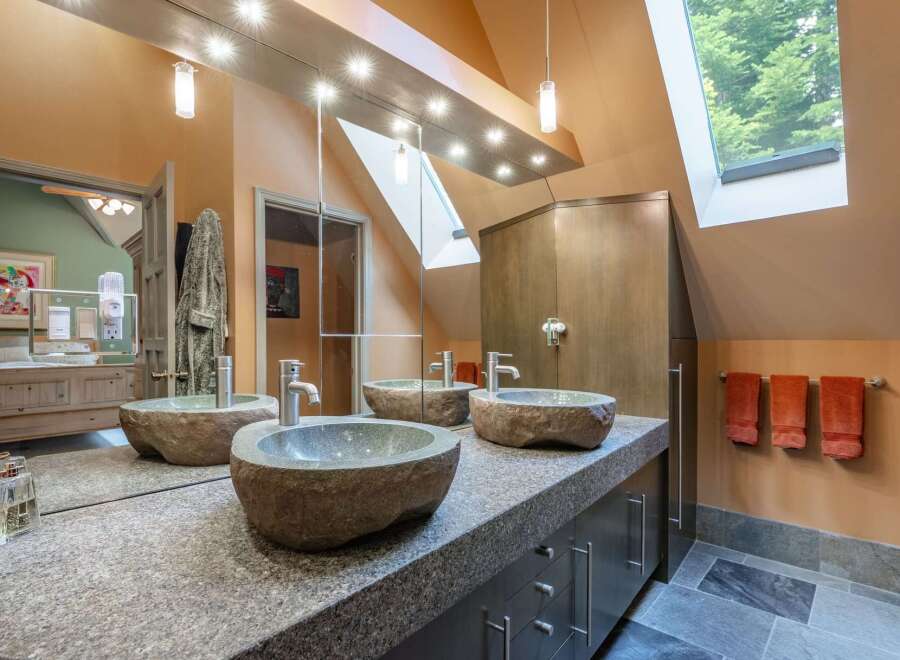 This luxurious bathroom features a unique double vanity with three stone vessel sinks, complemented by a granite countertop and dark wood cabinetry.