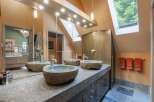 This luxurious bathroom features a unique double vanity with three stone vessel sinks, complemented by a granite countertop and dark wood cabinetry.
