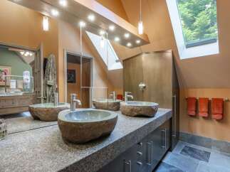 This luxurious bathroom features a unique double vanity with three stone vessel sinks, complemented by a granite countertop and dark wood cabinetry.