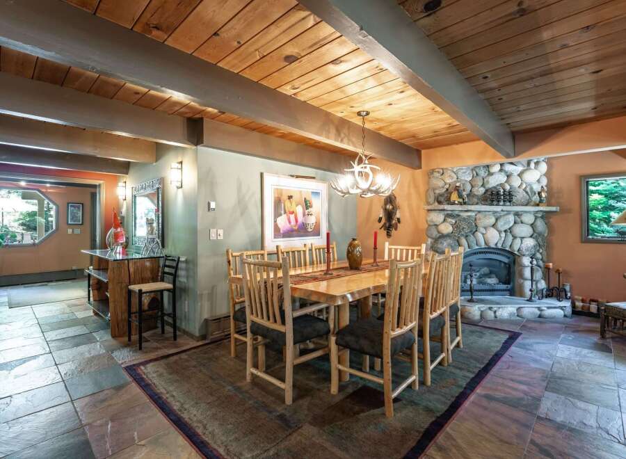 Experience rustic charm in this inviting dining area, featuring a grand stone fireplace and a warm, wood-paneled ceiling.