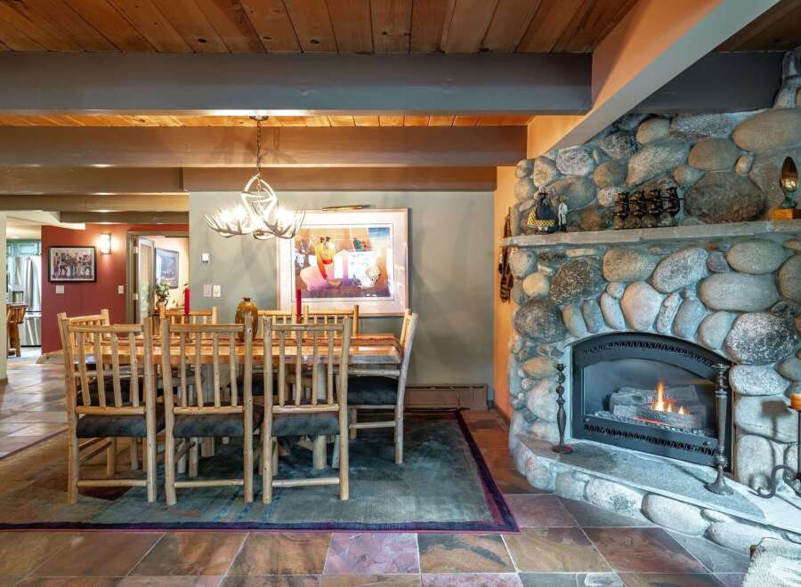 Experience rustic charm in this inviting dining area, featuring a grand stone fireplace and a unique antler chandelier.