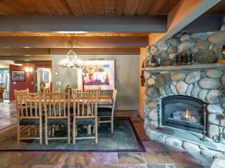 Experience rustic charm in this inviting dining area, featuring a grand stone fireplace and a unique antler chandelier.