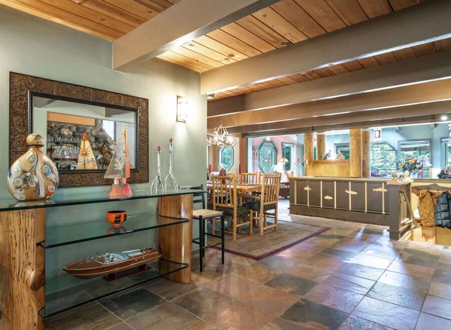 Experience rustic charm in this spacious dining and living area, featuring a stunning wood-beamed ceiling and a unique log-supported glass console table.