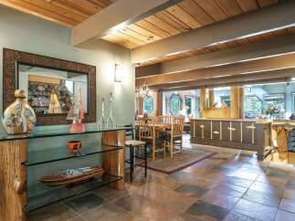 Experience rustic charm in this spacious dining and living area, featuring a stunning wood-beamed ceiling and a unique log-supported glass console table.