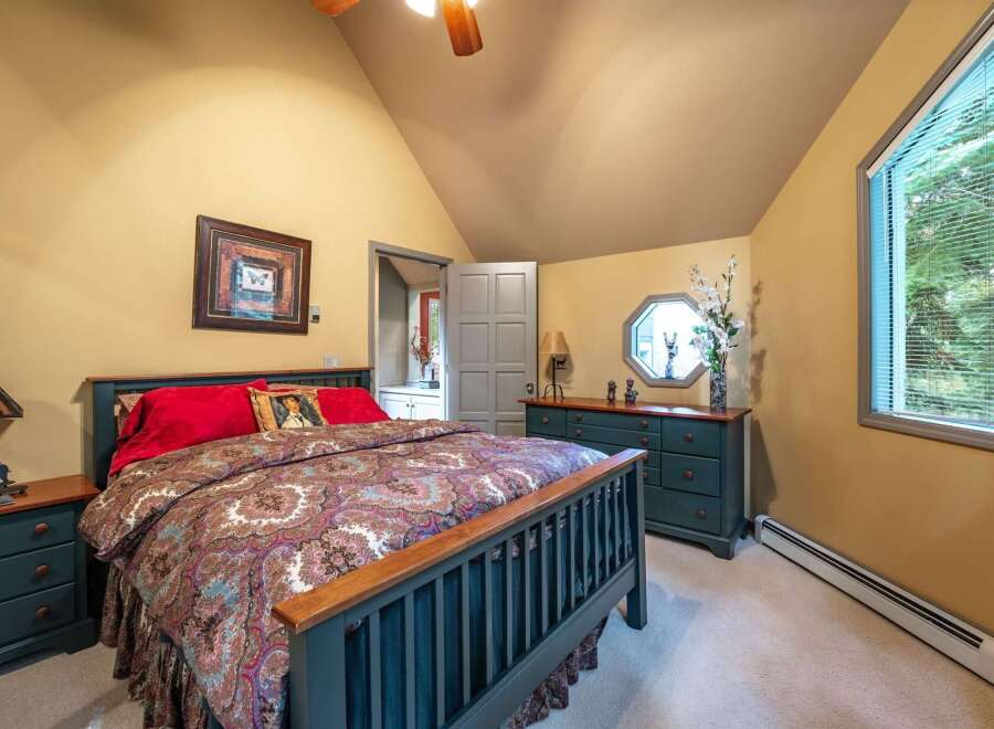 Discover this charming bedroom featuring a cozy queen-size bed adorned with a luxurious paisley comforter and vibrant red pillows.