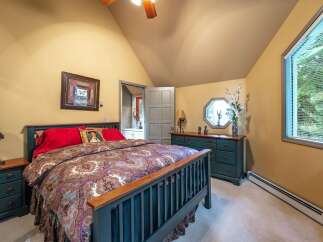 Discover this charming bedroom featuring a cozy queen-size bed adorned with a luxurious paisley comforter and vibrant red pillows.