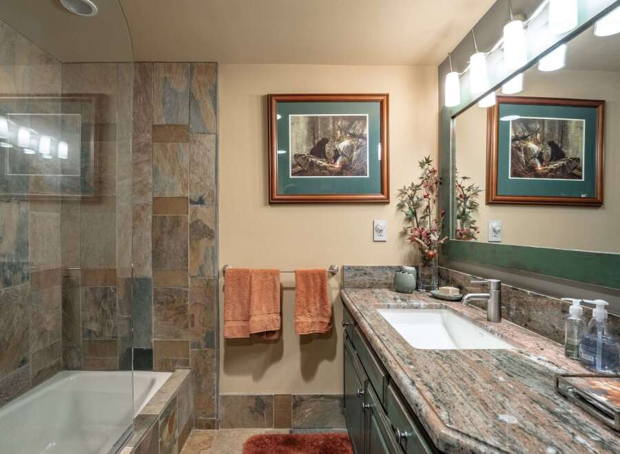This bathroom features a luxurious bathtub with slate tile surround, complemented by a spacious vanity with a granite countertop and a modern undermount sink.