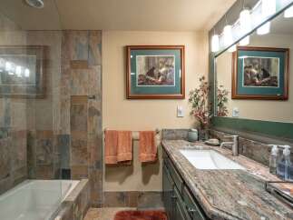 This bathroom features a luxurious bathtub with slate tile surround, complemented by a spacious vanity with a granite countertop and a modern undermount sink.