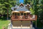 Nestled amidst tall pine trees, this charming home offers a spacious wooden deck perfect for outdoor entertaining, complete with umbrellas and seating.