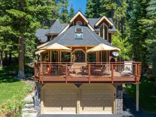 Nestled amidst tall pine trees, this charming home offers a spacious wooden deck perfect for outdoor entertaining, complete with umbrellas and seating.