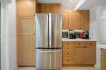 This modern kitchen features sleek stainless steel appliances, including a French door refrigerator, complemented by warm, natural wood cabinetry.