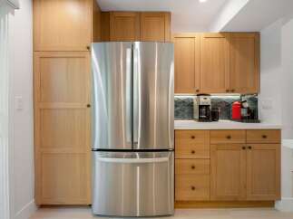This modern kitchen features sleek stainless steel appliances, including a French door refrigerator, complemented by warm, natural wood cabinetry.