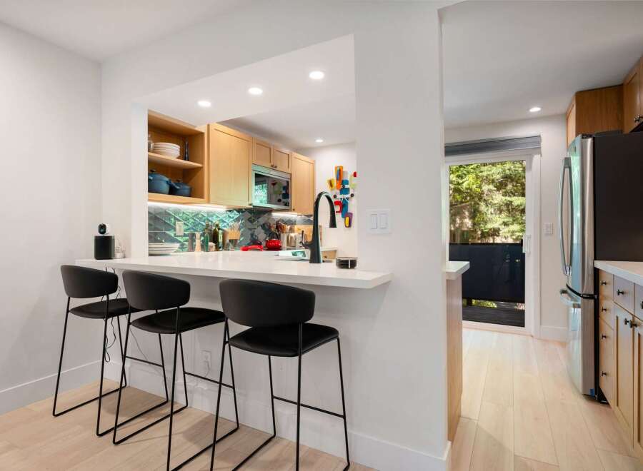 This modern kitchen features a sleek white breakfast bar with black bar stools, perfect for casual dining.