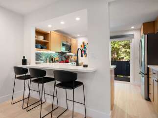 This modern kitchen features a sleek white breakfast bar with black bar stools, perfect for casual dining.