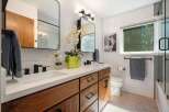 This modern bathroom features a sleek double vanity with warm wood cabinetry and a white quartz countertop.