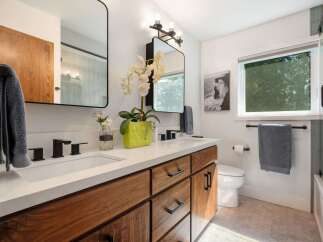 This modern bathroom features a sleek double vanity with warm wood cabinetry and a white quartz countertop.
