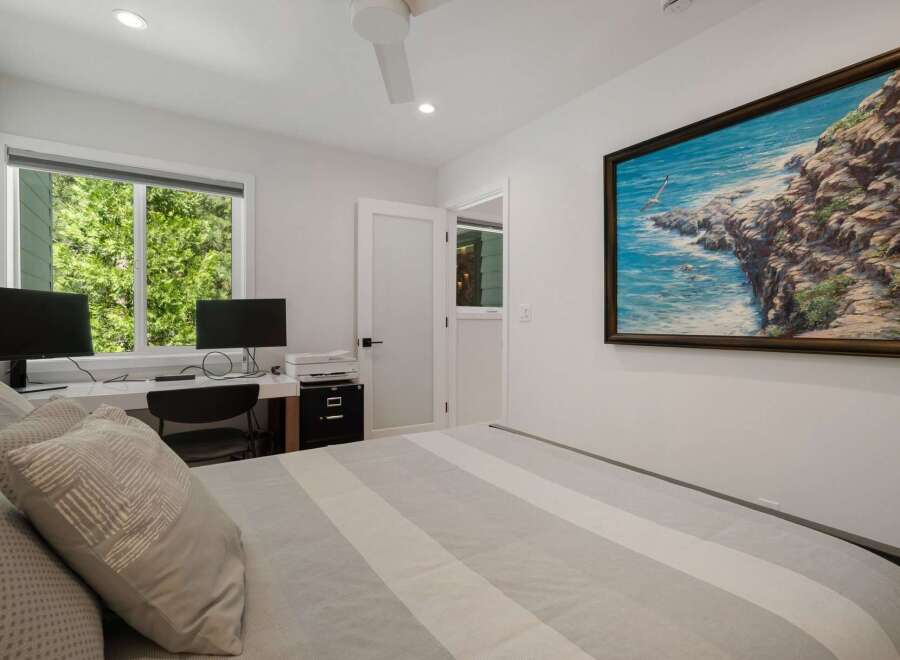 This bedroom features a comfortable bed with striped bedding and a large painting of a coastal scene above it.