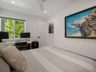 This bedroom features a comfortable bed with striped bedding and a large painting of a coastal scene above it.