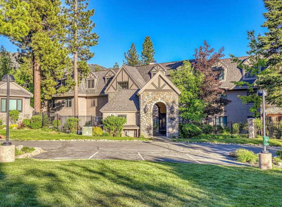 Discover this charming property featuring a stone-arched entryway leading to a multi-story building surrounded by lush greenery and mature trees.