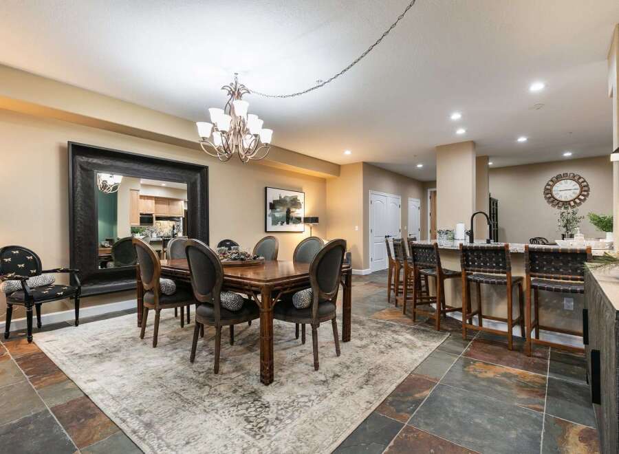 This elegant dining room features a large wooden table with upholstered chairs, complemented by a striking oversized mirror and a modern chandelier.