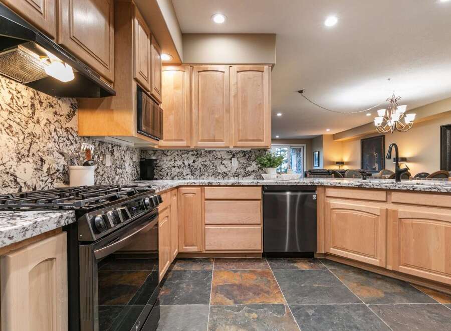 This modern kitchen features sleek stainless steel appliances, including a gas range and dishwasher, complemented by elegant granite countertops and a striking marble backsplash.