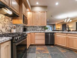This modern kitchen features sleek stainless steel appliances, including a gas range and dishwasher, complemented by elegant granite countertops and a striking marble backsplash.