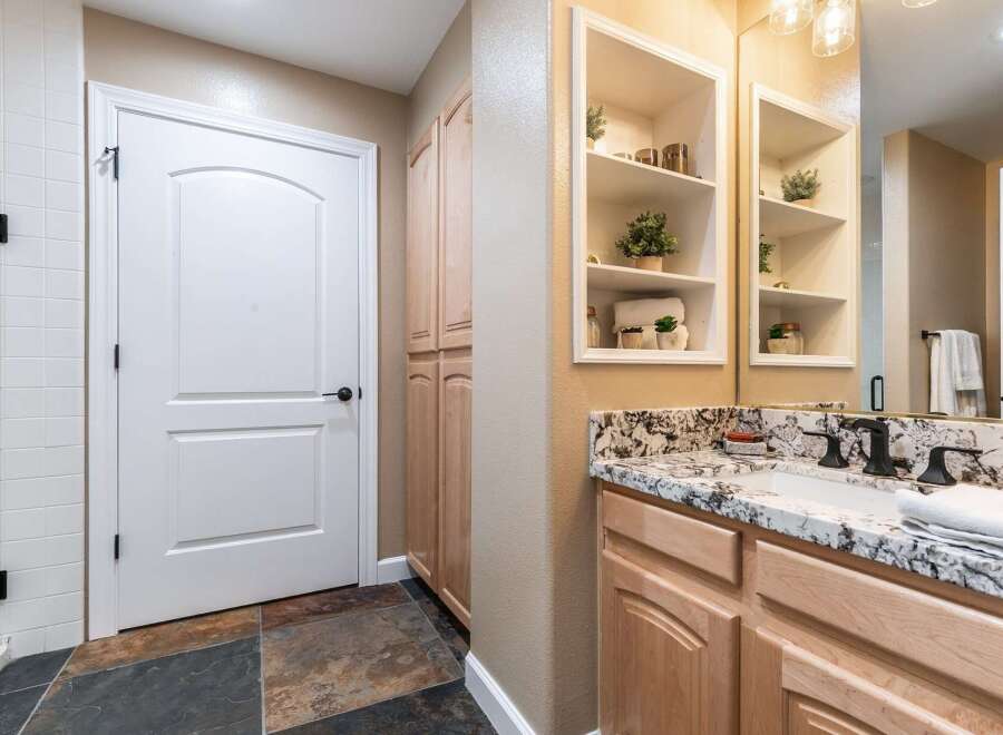 This bathroom features a white arched door leading to a tiled shower area and a tall wooden cabinet.