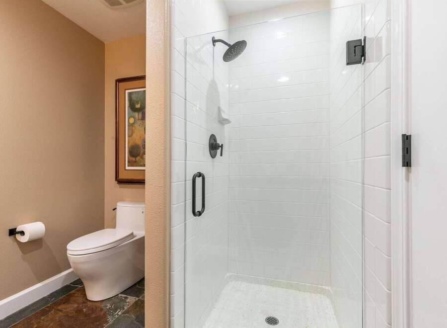 Experience modern comfort in this bathroom featuring a sleek, white tiled walk-in shower with black fixtures.